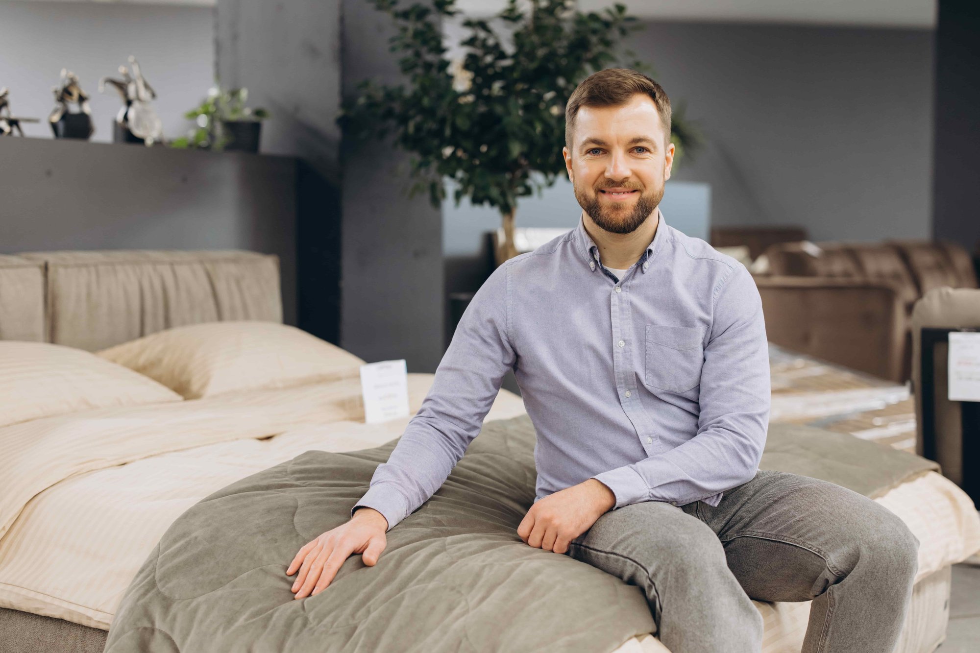 Berater sitzt auf einem Bett im Bettenstudio und präsentiert hochwertige Matratzen