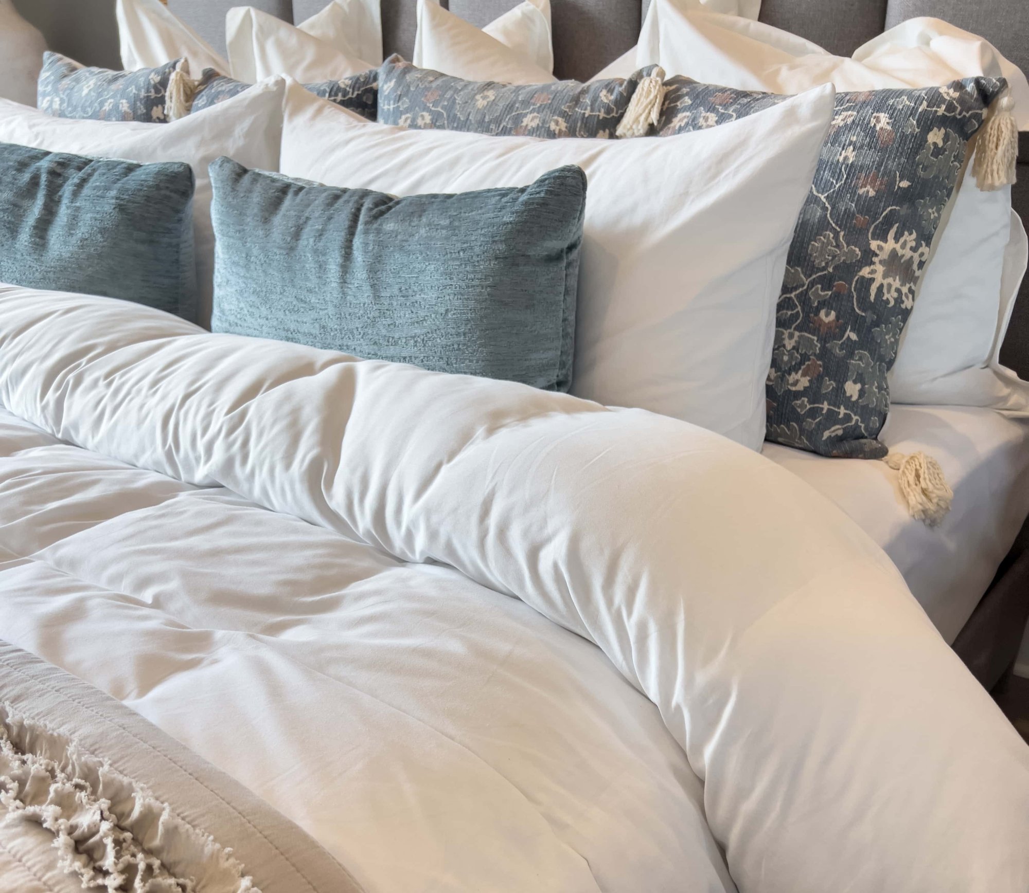 Detailaufnahme eines Bettes mit weißen und blauen Kissen und hochwertiger weißer Bettwäsche